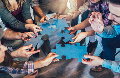 im-team-arbeiten Gesund Führen - Team-Mitarbeitende fügen Teile zu einem Puzzle zusammen